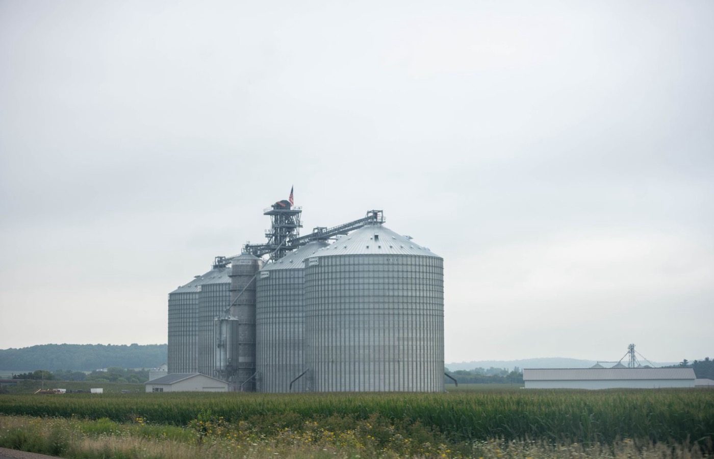 Grain bins standing over Midwest farmland under an overcast sky